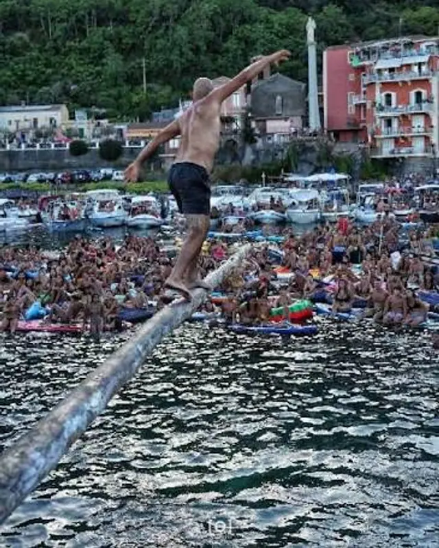L'antenna a mare durante la festa: il pubblico in acqua e il concorrente sul tronco